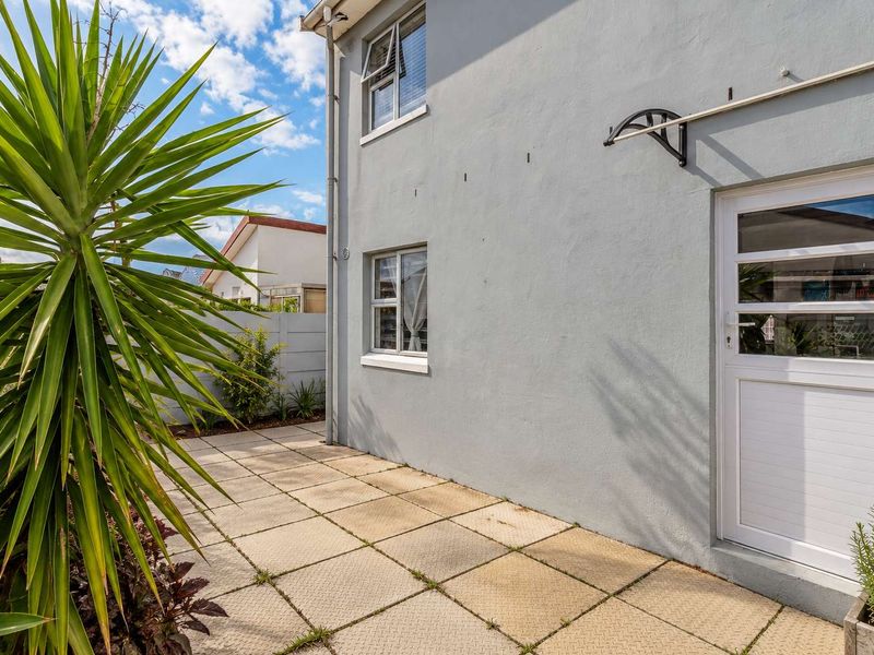 A rear exterior view of the apartment featuring a paved patio area, external door access, and aluminium window frames.