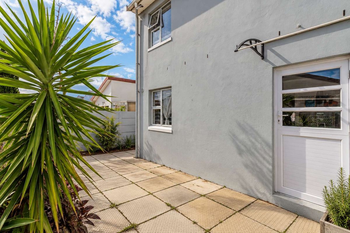 A rear exterior view of the apartment featuring a paved patio area, external door access, and aluminium window frames.