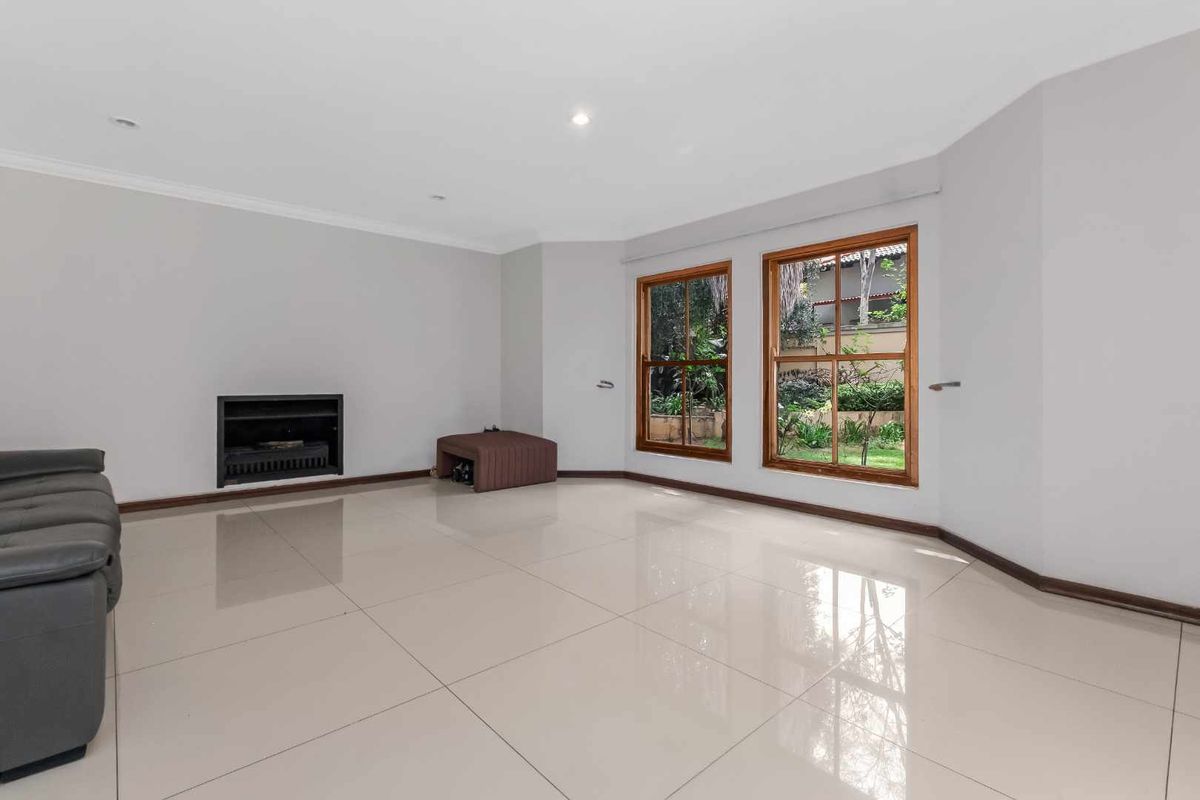 Spacious living room featuring large wooden-framed windows, polished tiled flooring, and a built-in fireplace, offering a bright and neutral canvas for interior design.