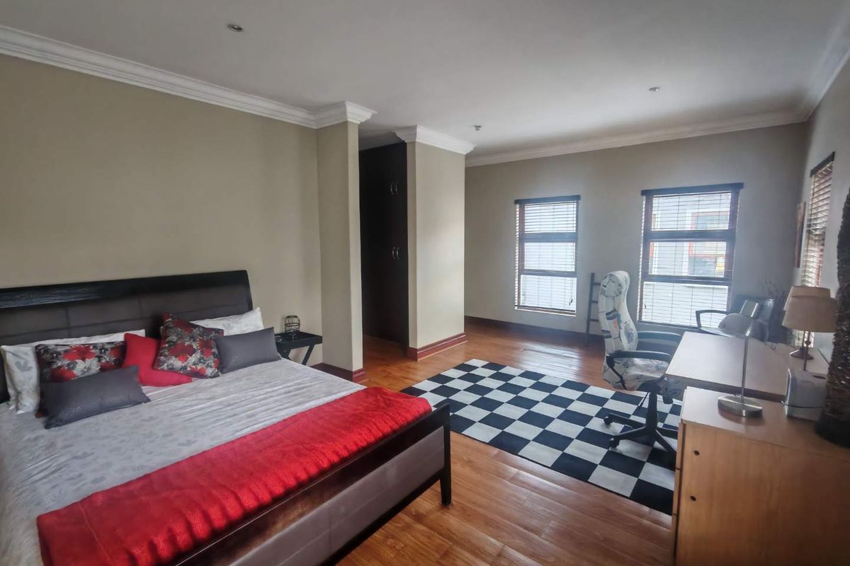 Spacious bedroom featuring warm-toned laminate flooring, crown molding, and built-in cupboards, offering a comfortable and functional living space.