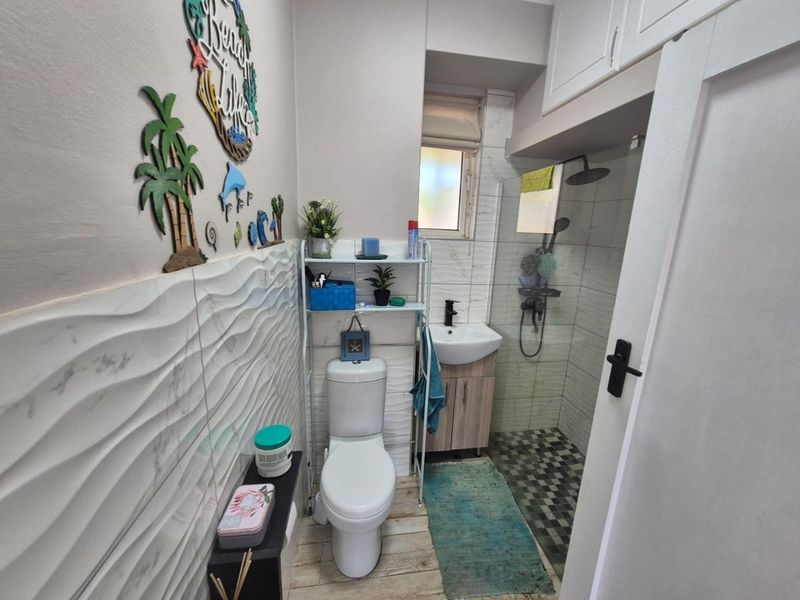 Compact bathroom featuring a modern toilet, vanity basin, and a glass-enclosed shower with textured wall tiling and overhead storage cabinetry.