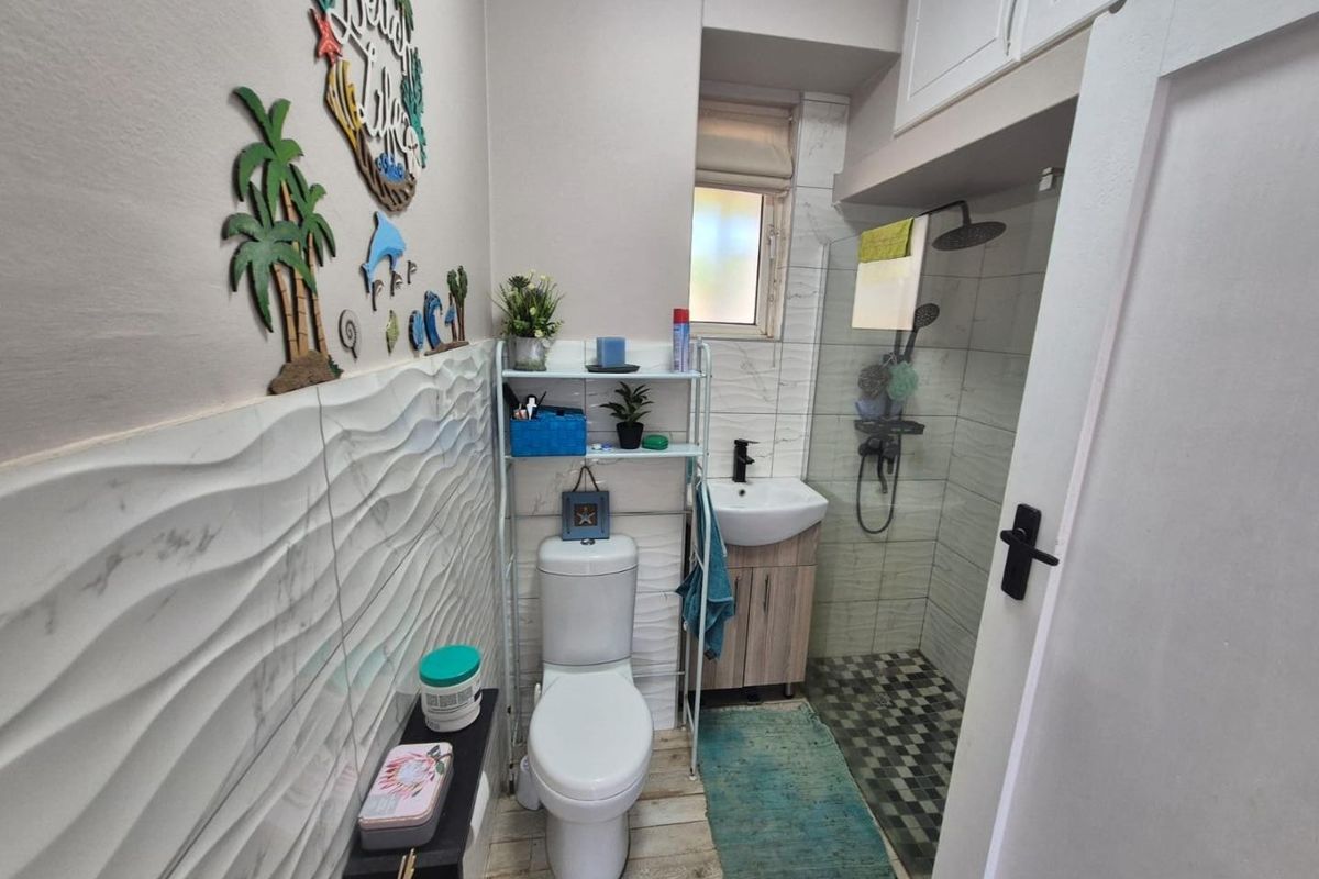 Compact bathroom featuring a modern toilet, vanity basin, and a glass-enclosed shower with textured wall tiling and overhead storage cabinetry.