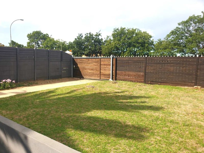 A well-maintained private garden featuring a neat lawn, paved walkway, and secure timber slat fencing with integrated security spikes.