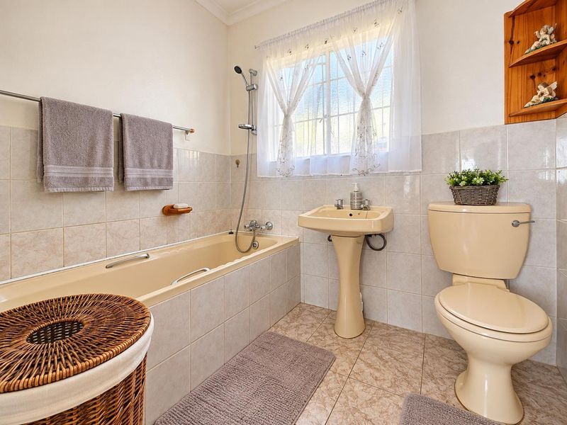 A functional bathroom featuring a bathtub with handheld shower, pedestal basin, and toilet, finished with neutral wall and floor tiling.
