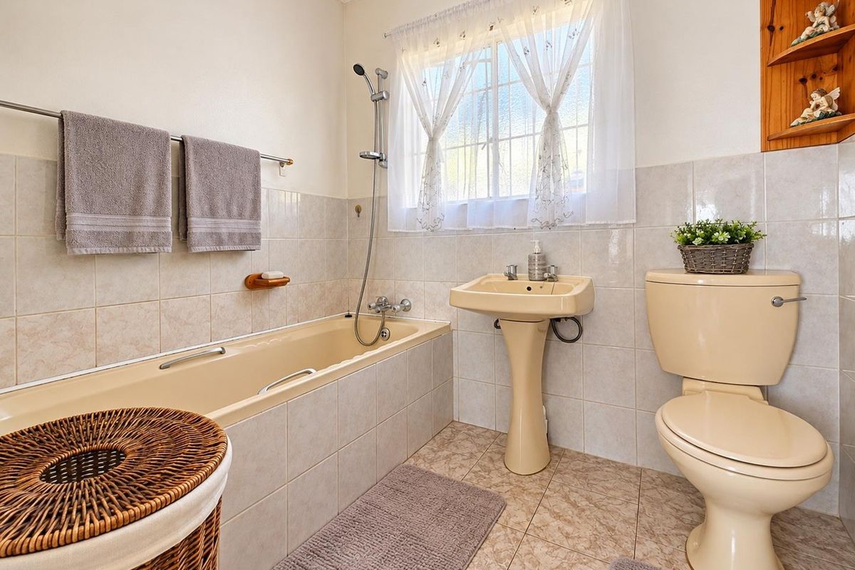 A functional bathroom featuring a bathtub with handheld shower, pedestal basin, and toilet, finished with neutral wall and floor tiling.