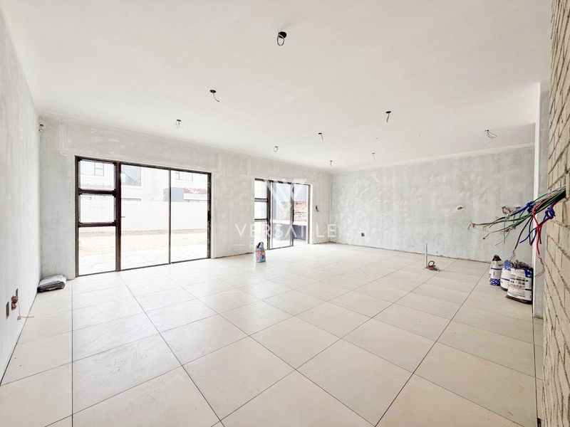 Spacious open-plan living area in shell condition, featuring large aluminium sliding doors, tiled flooring, and unfinished walls awaiting final finishes and electrical installation.