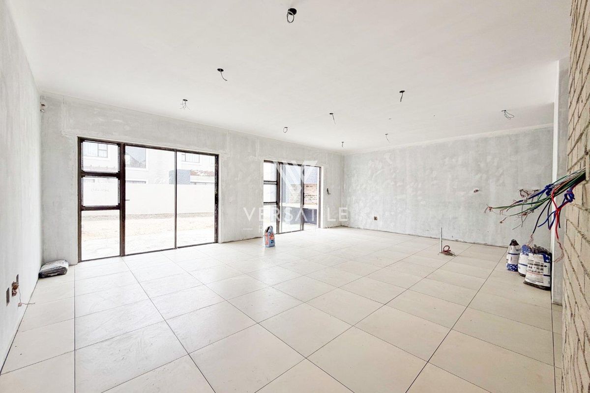 Spacious open-plan living area in shell condition, featuring large aluminium sliding doors, tiled flooring, and unfinished walls awaiting final finishes and electrical installation.