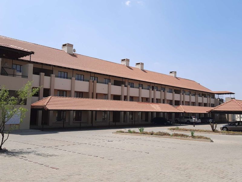 Exterior view of a multi-story apartment complex featuring a tiled roof, covered parking bays, and a paved driveway area.