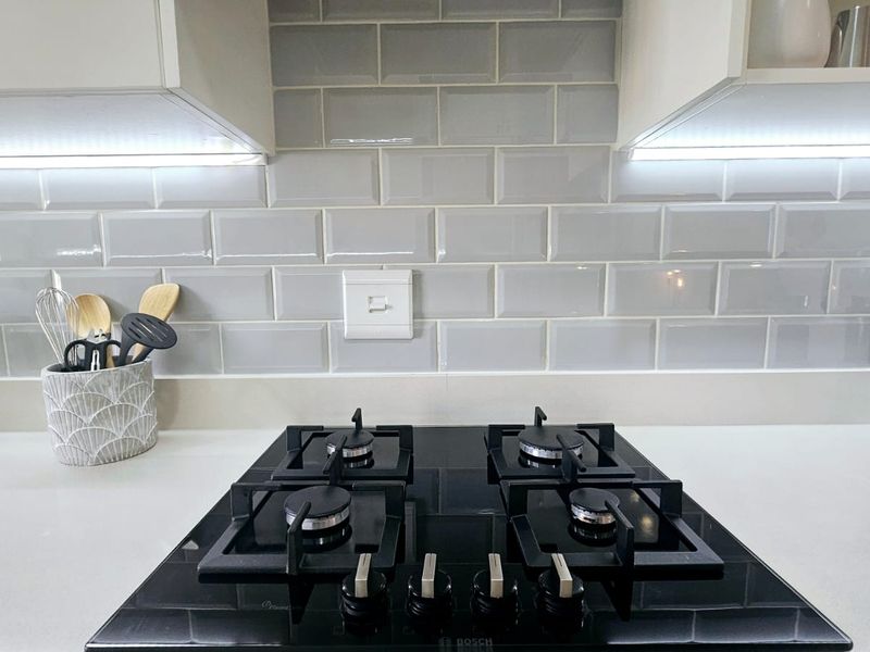 Modern kitchen featuring a sleek black gas hob, white quartz countertops, and a stylish grey subway tile backsplash with integrated under-cabinet lighting.