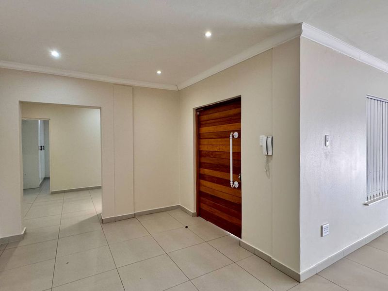 A bright and spacious entrance hall featuring neutral tiled flooring, recessed downlighting, and a solid wooden front door with an integrated intercom system.