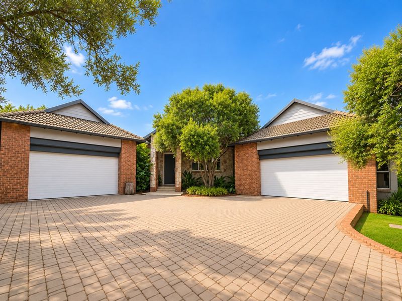 A well-maintained front exterior featuring a spacious paved driveway, double garage, and attractive brick and stone facade with established landscaping.