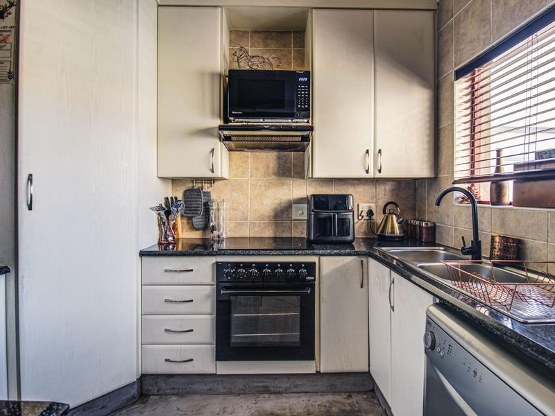 Compact kitchen featuring built-in cabinetry, granite countertops, integrated oven and hob, and a double sink with a tiled backsplash.