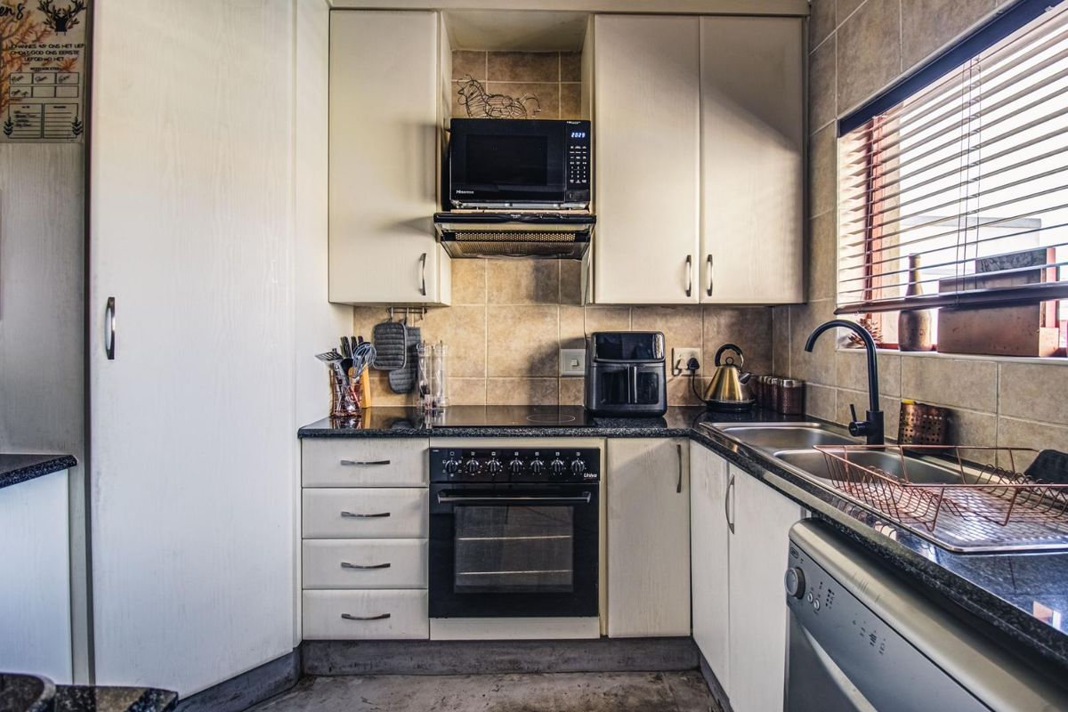 Compact kitchen featuring built-in cabinetry, granite countertops, integrated oven and hob, and a double sink with a tiled backsplash.