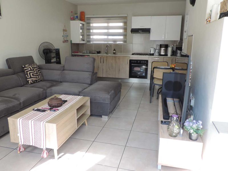Open-plan living area featuring a functional kitchen with built-in cabinetry, oven, and hob, seamlessly connected to a tiled lounge space.