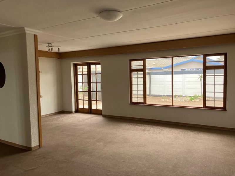 Spacious, empty living area featuring timber-framed windows and french doors leading to the exterior, providing a blank canvas for interior design.