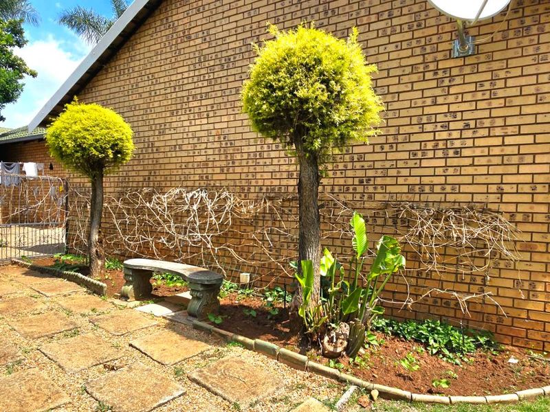A view of the rear exterior featuring a face brick wall, paved garden path, and established landscaping.