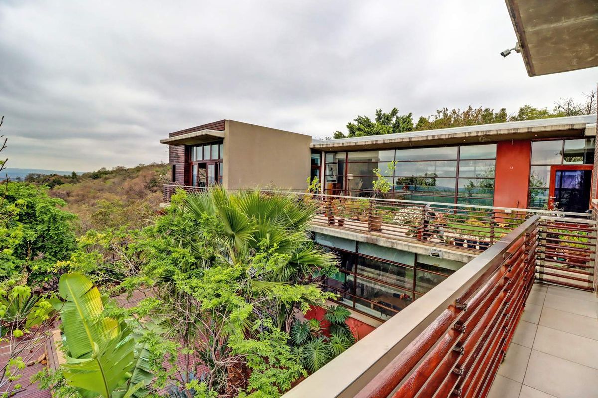 A modern multi-level exterior view featuring expansive glass facades, timber accents, and a spacious balcony overlooking the surrounding landscape.