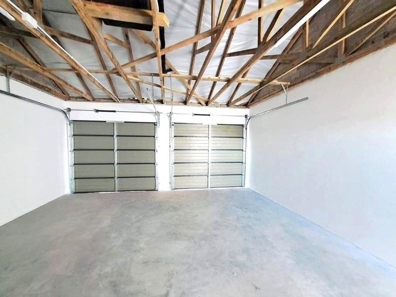 A spacious double garage featuring exposed timber roof trusses, concrete flooring, and two functional garage doors.