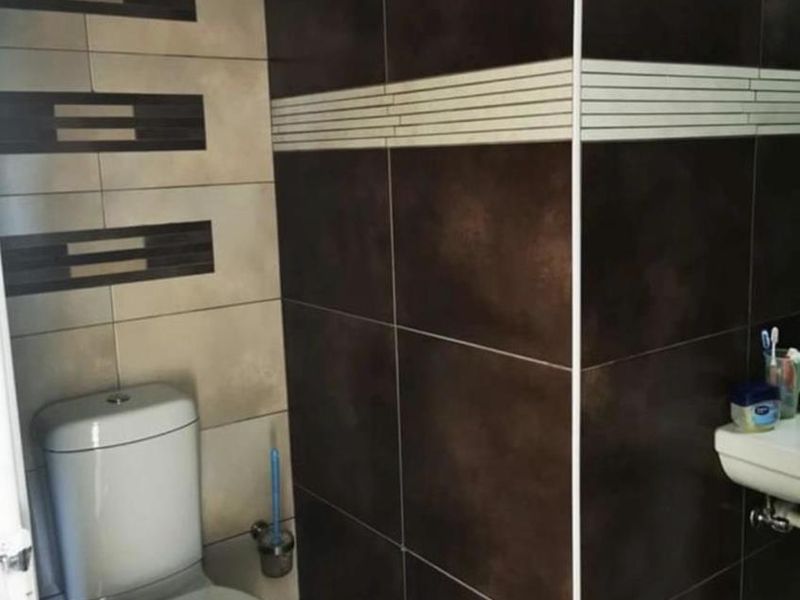 A compact bathroom featuring dark and light contrasting wall tiles, a standard white toilet, and a wall-mounted washbasin.