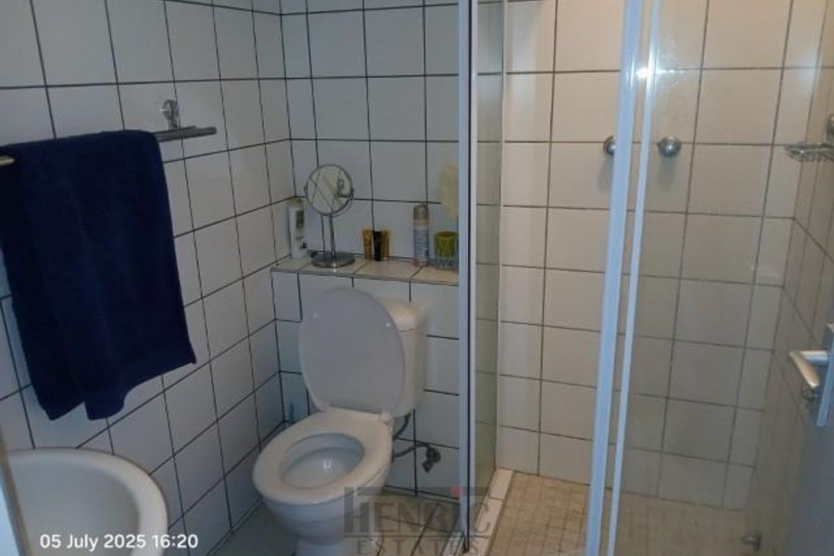 A functional bathroom featuring a white toilet, a glass-enclosed shower, and full-height wall tiling.