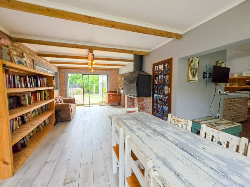 Open-plan living and dining area featuring exposed timber ceiling beams, a brick feature wall, a built-in fireplace, and direct access to the rear garden.