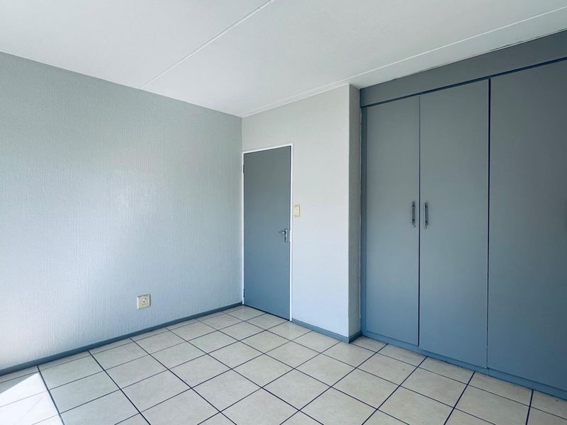 An empty bedroom featuring neutral tiled flooring and built-in grey cupboards, offering a clean and functional space ready for personalization.