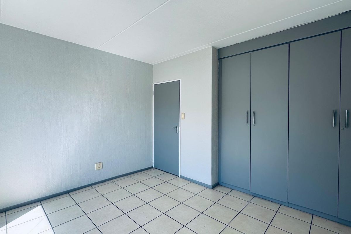 An empty bedroom featuring neutral tiled flooring and built-in grey cupboards, offering a clean and functional space ready for personalization.