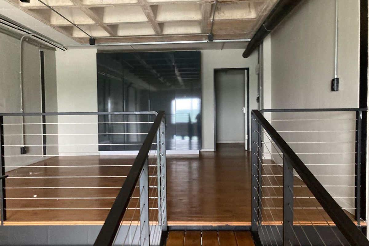 An industrial-style mezzanine level featuring exposed concrete waffle ceiling, timber flooring, and modern cable railing overlooking the lower floor.