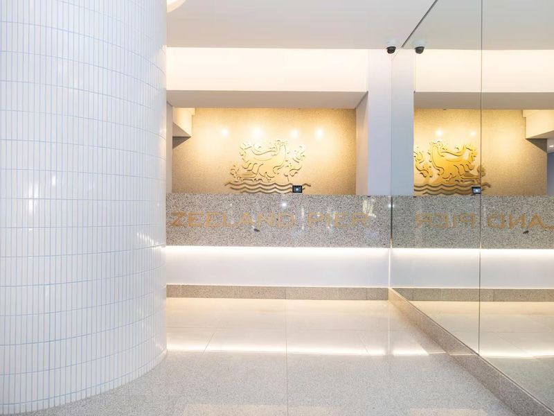 A modern, well-maintained apartment building entrance lobby featuring a granite reception desk, tiled architectural column, and large wall mirror.