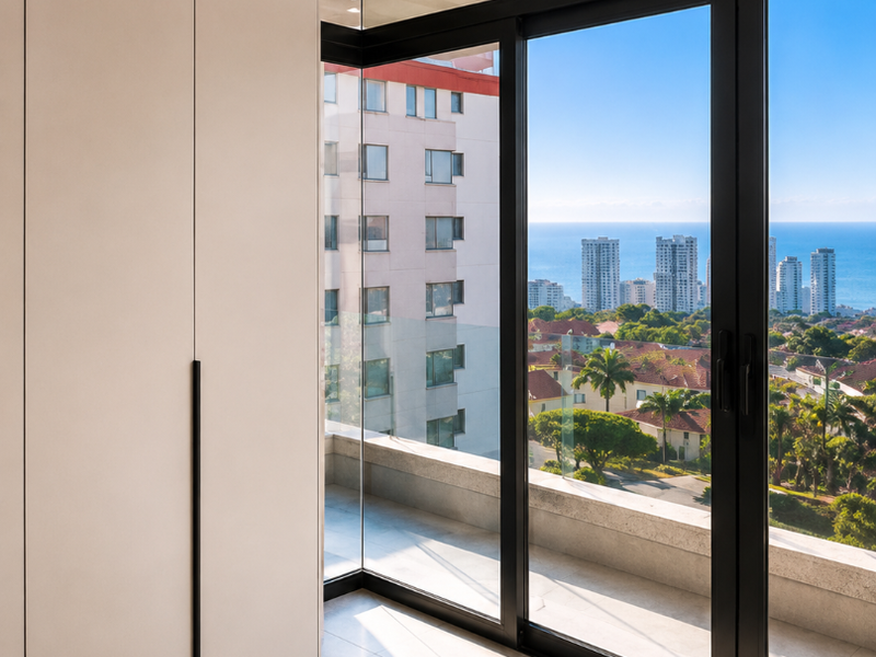 Modern bedroom featuring sleek built-in cupboards, large floor-to-ceiling windows, and sliding doors opening to a balcony with expansive coastal and city views.