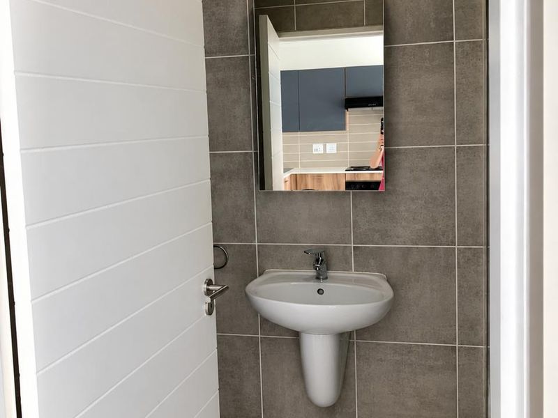 A clean, modern bathroom featuring a pedestal basin, chrome mixer tap, and neutral grey ceramic wall and floor tiling.