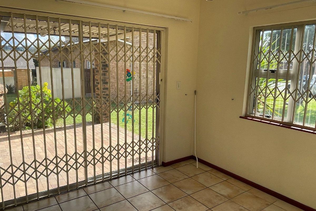 An empty living area featuring tiled flooring, security gates on the sliding door and window, and direct access to the rear patio.