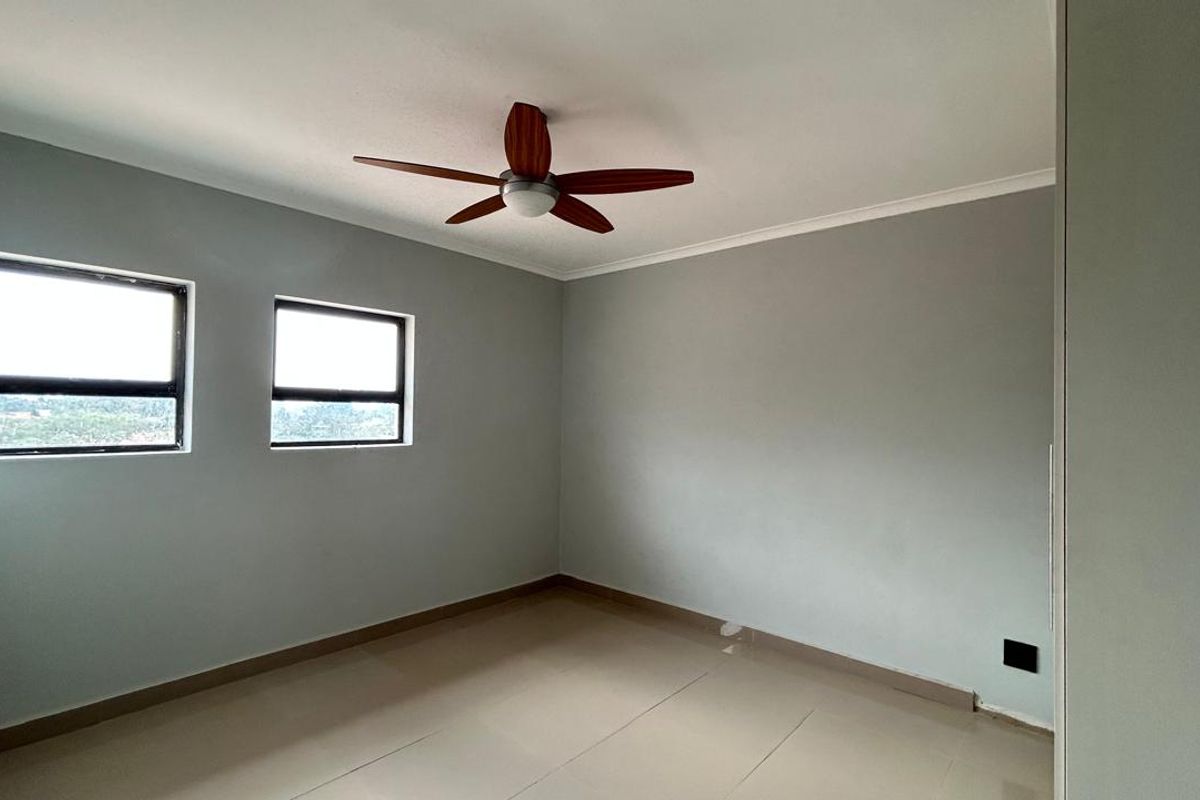 A bright, empty bedroom featuring neutral wall paint, tiled flooring, and a ceiling fan.