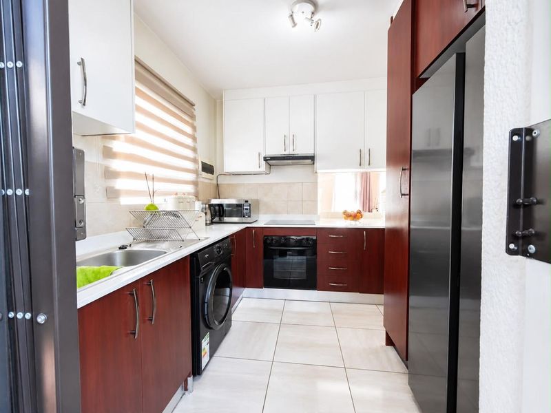 A functional kitchen featuring two-tone cabinetry, integrated appliances including an oven and hob, tiled flooring, and a neutral tiled backsplash.