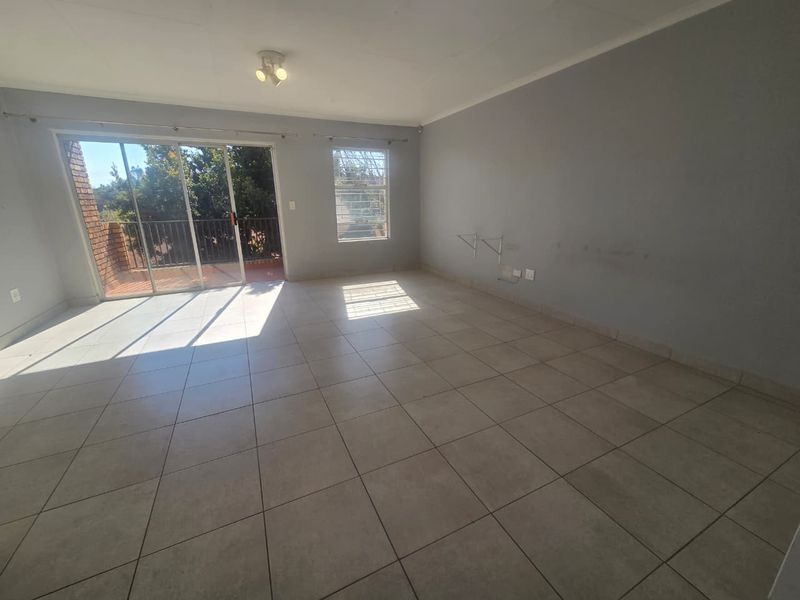 Spacious, empty living area featuring neutral tiled flooring, large sliding glass doors leading to a balcony, and ample natural light.