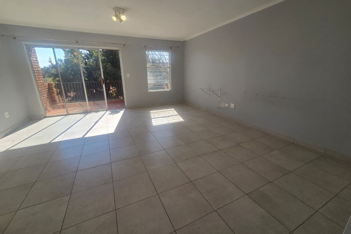 Spacious, empty living area featuring neutral tiled flooring, large sliding glass doors leading to a balcony, and ample natural light.