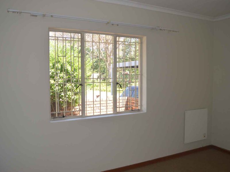 A vacant bedroom featuring neutral walls, a wall-mounted heater, and a window fitted with security bars.
