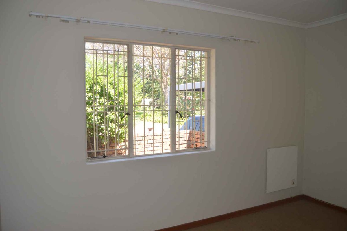 A vacant bedroom featuring neutral walls, a wall-mounted heater, and a window fitted with security bars.