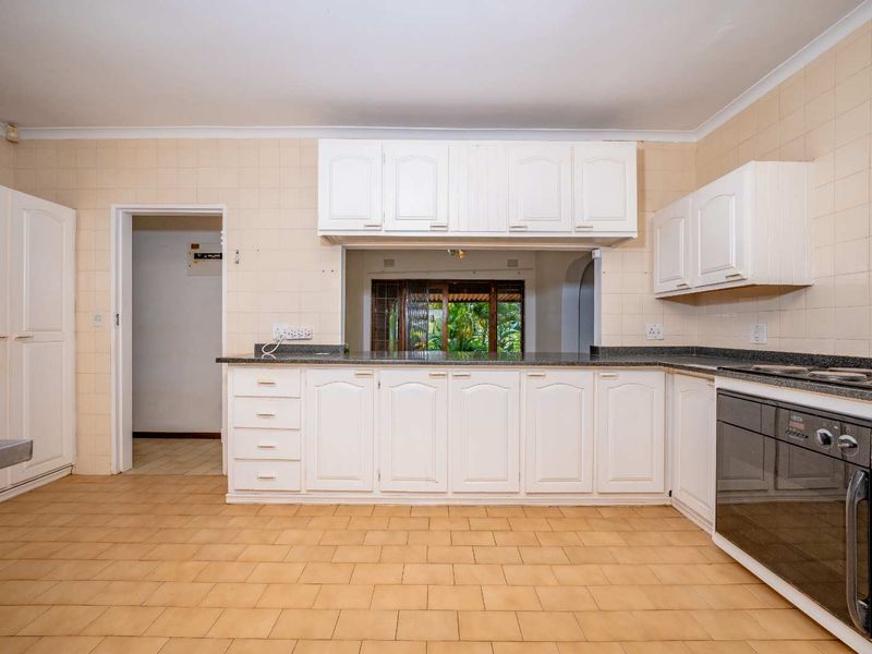 A spacious, empty kitchen featuring white built-in cabinetry, granite countertops, and a built-in oven, offering a functional layout ready for modernization.