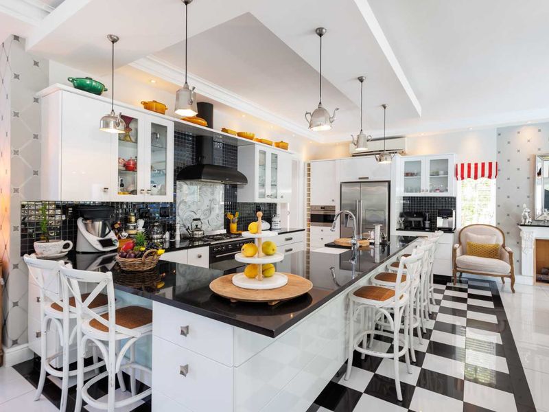 A modern, well-appointed kitchen featuring a large central island, high-gloss cabinetry, black granite countertops, and a striking checkered floor design.