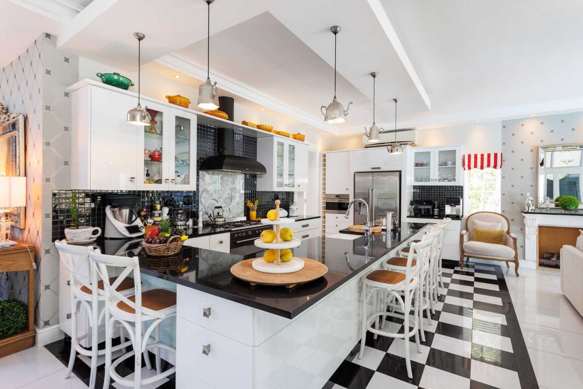 A modern, well-appointed kitchen featuring a large central island, high-gloss cabinetry, black granite countertops, and a striking checkered floor design.