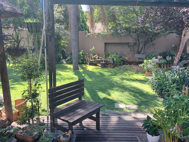 A lush, well-maintained private garden featuring a timber deck, established trees, and a secure perimeter wall.