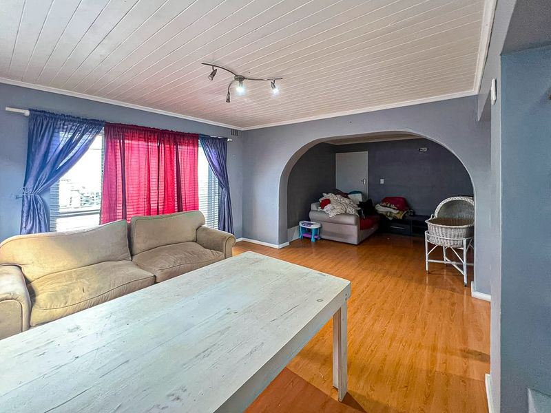 Spacious living area featuring laminate flooring, a timber panelled ceiling, and a distinctive architectural archway connecting to an adjacent space.