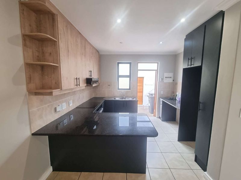 Modern kitchen featuring granite countertops, ample built-in cabinetry, tiled flooring, and direct access to the rear exterior.