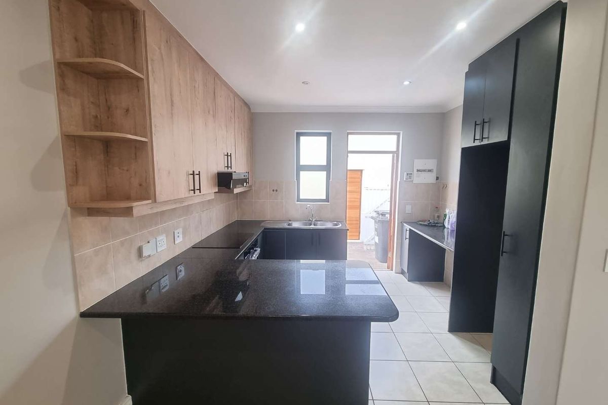 Modern kitchen featuring granite countertops, ample built-in cabinetry, tiled flooring, and direct access to the rear exterior.