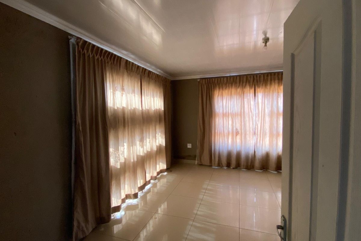 A bright, empty living room featuring large windows with curtains and neutral tiled flooring, offering a versatile space ready for personalization.