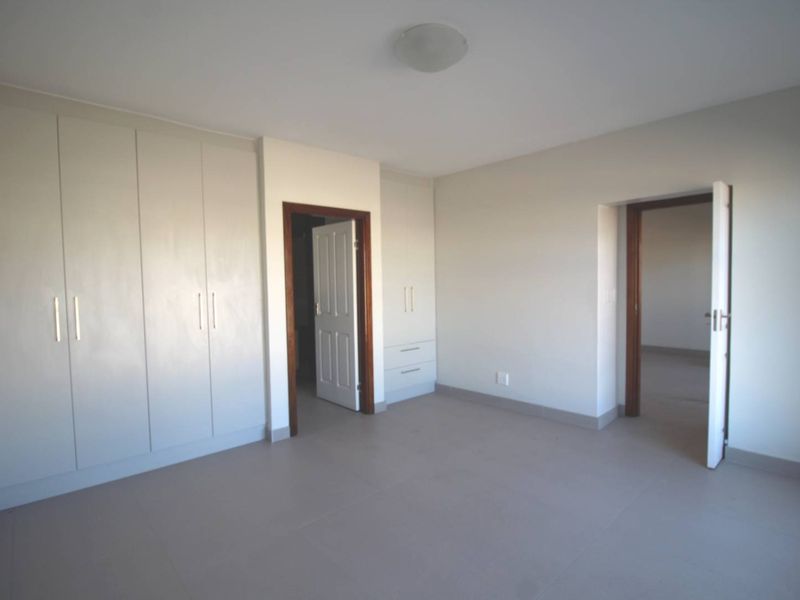 A spacious, empty bedroom featuring neutral tiled flooring and extensive built-in cupboard storage with modern hardware.