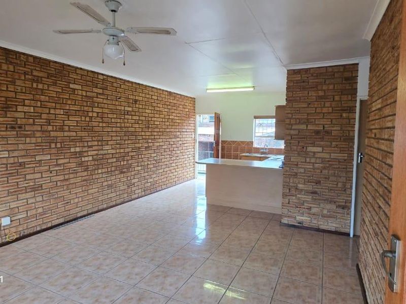 Spacious open-plan living and kitchen area featuring exposed brick walls, ceramic tile flooring, and a functional breakfast bar layout.