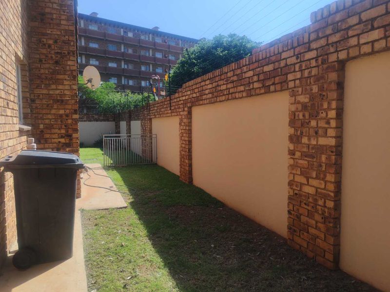 A side garden area featuring a brick boundary wall with integrated electric fencing and a concrete pathway leading to a small lawn.