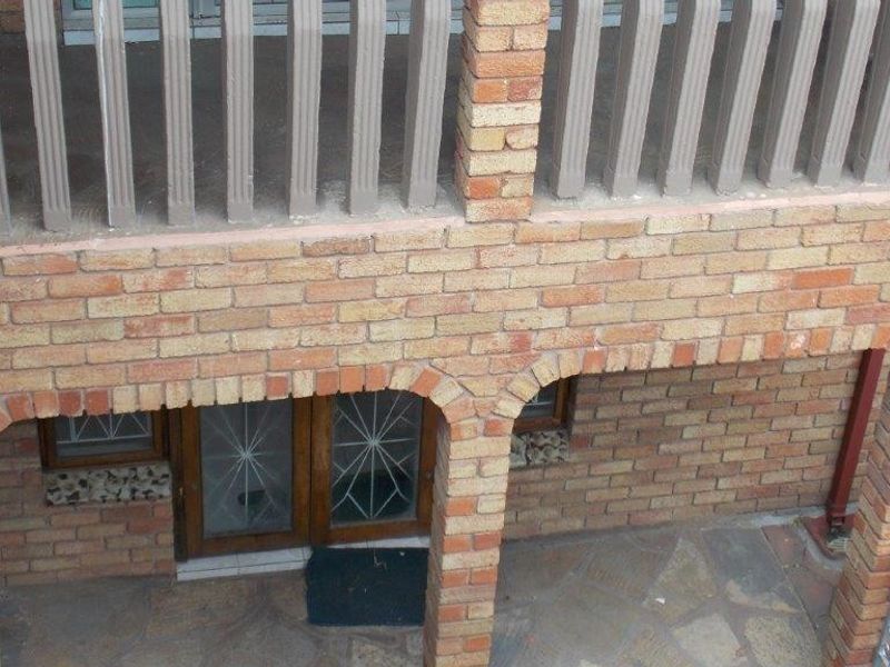 A view of the rear exterior featuring a brick facade, arched columns, stone paved patio area, and an upper-level balcony with railings.